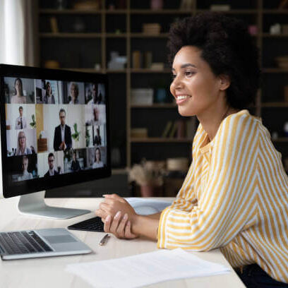 Happy African American remote employee talking on video conference call to colleagues, sitting at computer monitor, speaking to audience, attending virtual business meeting, negotiations, seminar